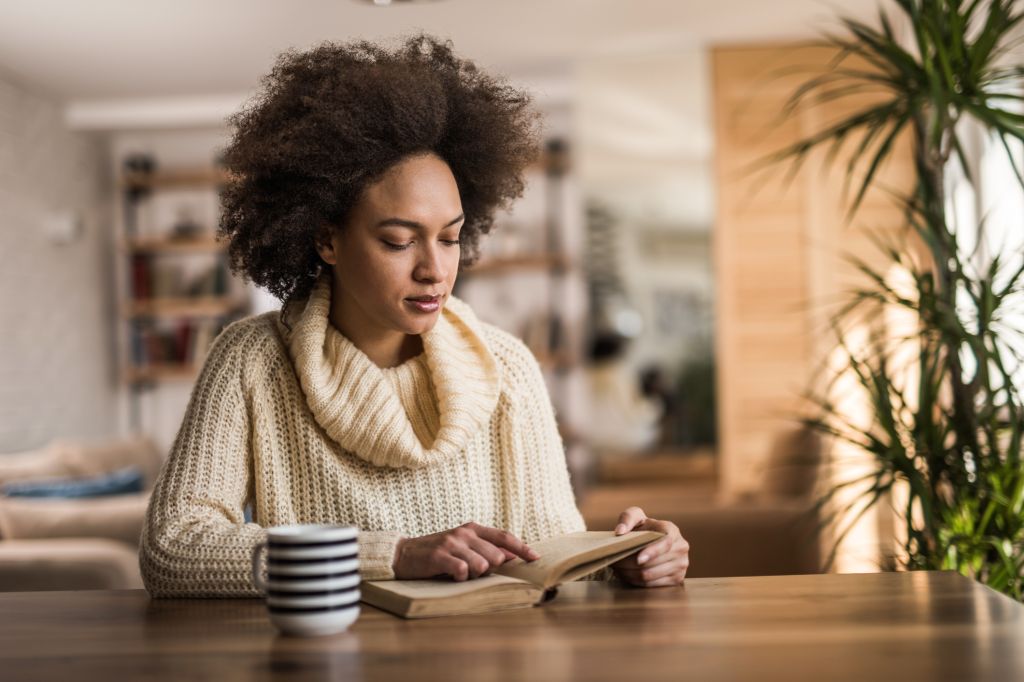 Beautiful black woman reading a book at home.